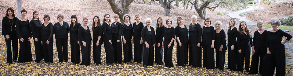 Photo of Voci singers dressed in black, standing outdoors in front of trees